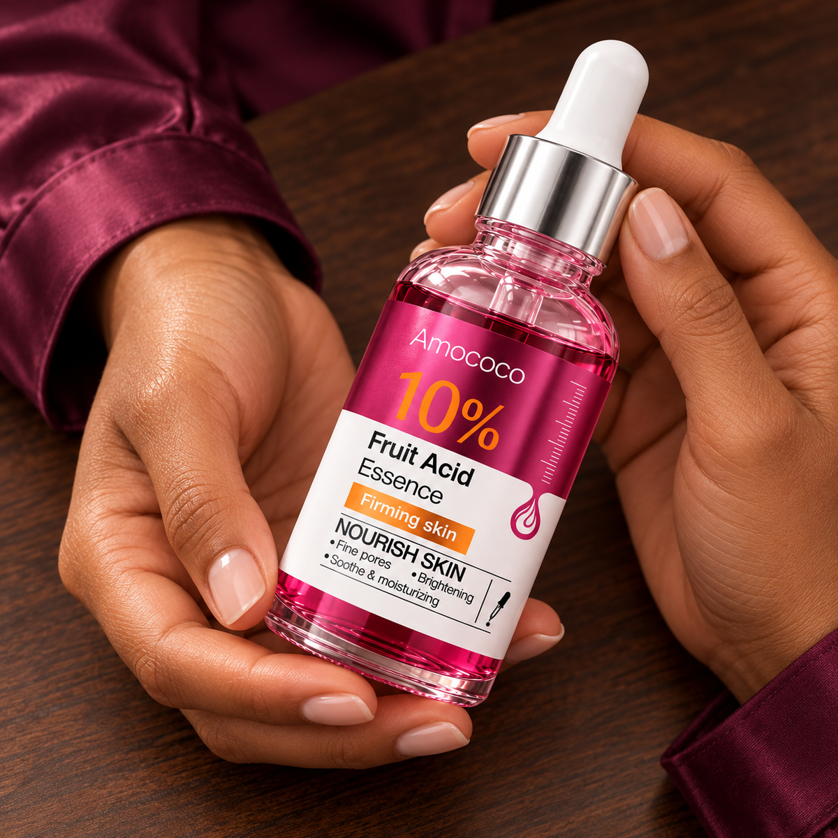 Amococo 10% Fruit Acid Essence closed bottle label held in matching model hands over dark walnut