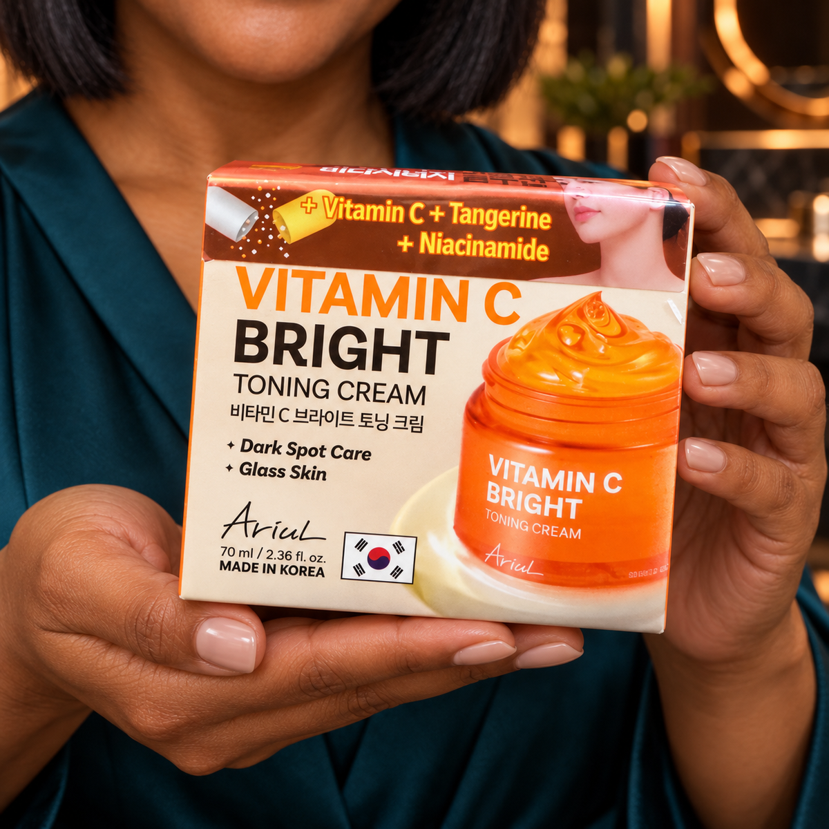 Close handheld front-label detail of the closed Ariul Vitamin C Bright Toning Cream 70 ml carton, shown by the same adult woman