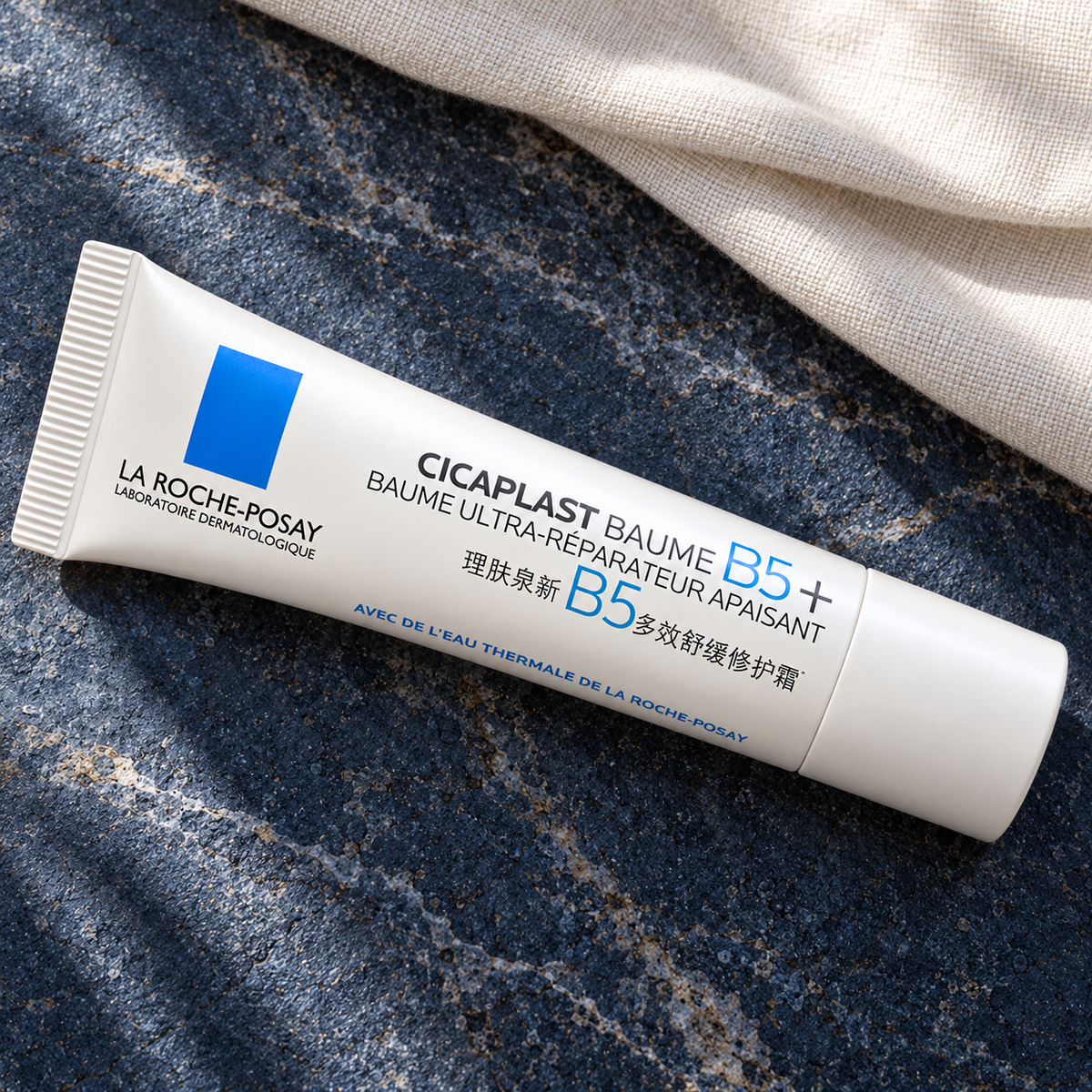 Closed La Roche-Posay Cicaplast Baume B5+ tube with French and Chinese labeling, shown diagonally on blue stone
