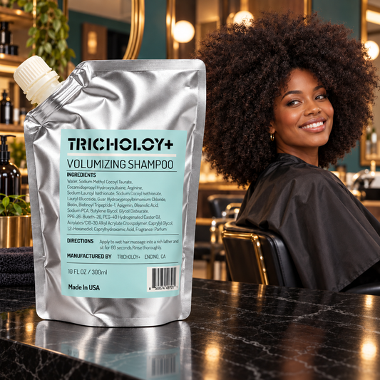 TRICHOLOY+ Volumizing Shampoo 300 ml silver pouch on polished black stone in a salon with a smiling adult woman wearing a full natural afro. AI-created lifestyle setting.